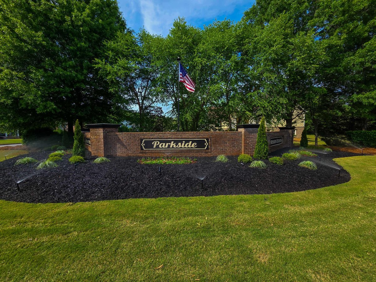 Parkside neighborhood entrance sign with brick structure, landscaping, and American flag under green trees